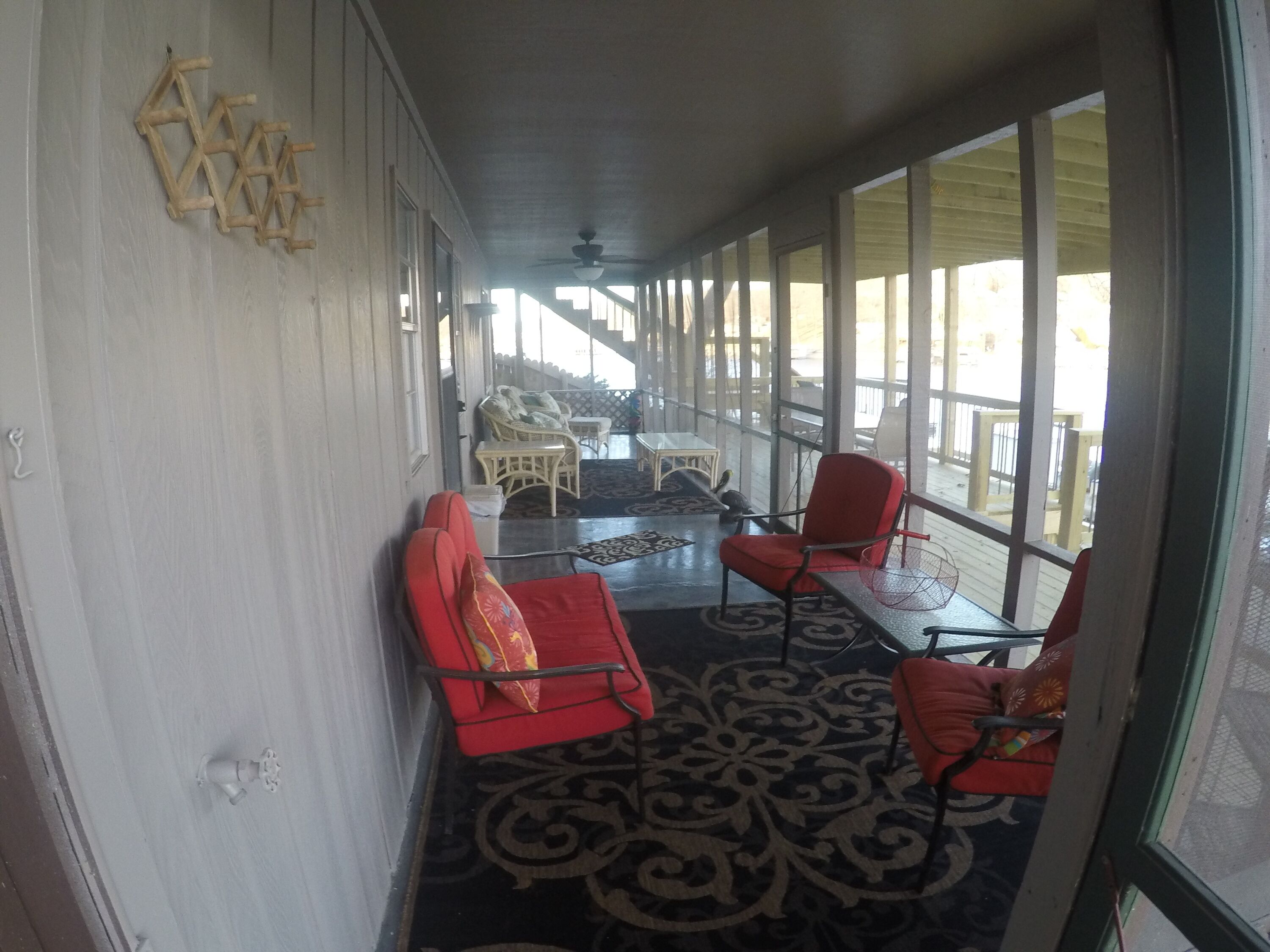 A covered porch with red chairs, a table, and wicker furniture.