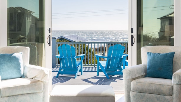 Een balkon met twee blauwe Adirondack-stoelen en een witte poef, met uitzicht op de kust.
