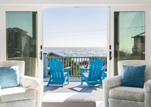 Un balcón con dos sillas Adirondack azules y un reposapiés blanco, con vista al mar.