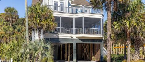 A two-story house with a balcony, surrounded by palm trees and a white picket fence.