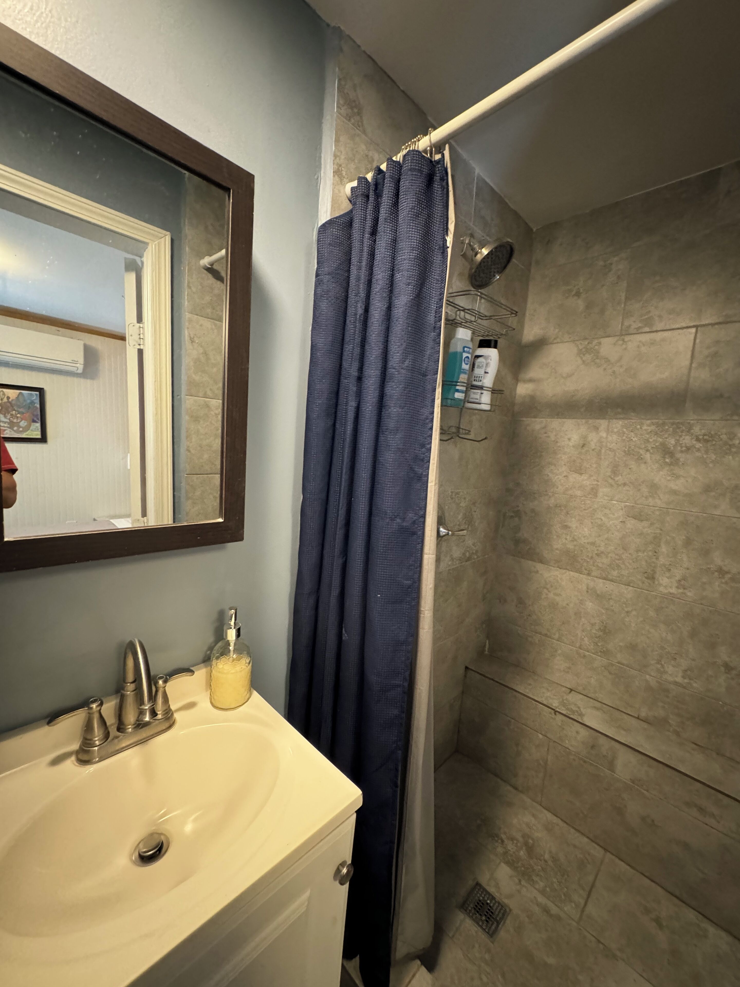 A bathroom with a white sink, a mirror, and a shower with a blue curtain.