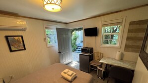 Habitación de hotel compacta con cama, escritorio, microondas, televisor y un pequeño cesto de basura.
