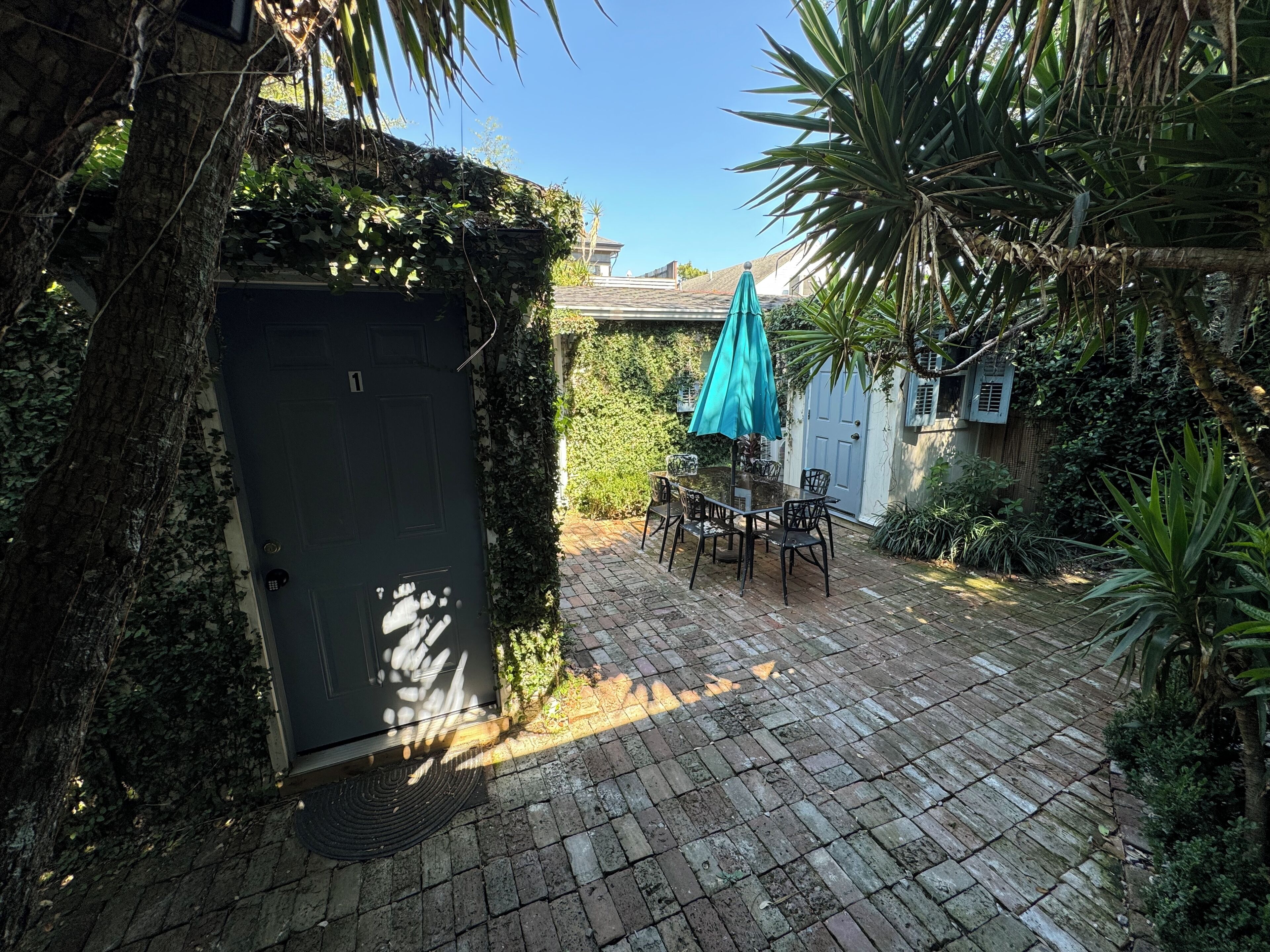 Une terrasse avec une table et des chaises, entourée de verdure et donnant sur une porte.