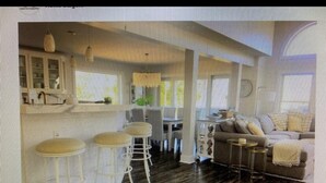 A spacious living area with a large sofa, a dining table, and a kitchen area with white cabinets and bar stools. - 5-Star Oceanblock Sleeps 18! Luxury Beach Vacation Home Private Beach Community  (Bethany Beach)