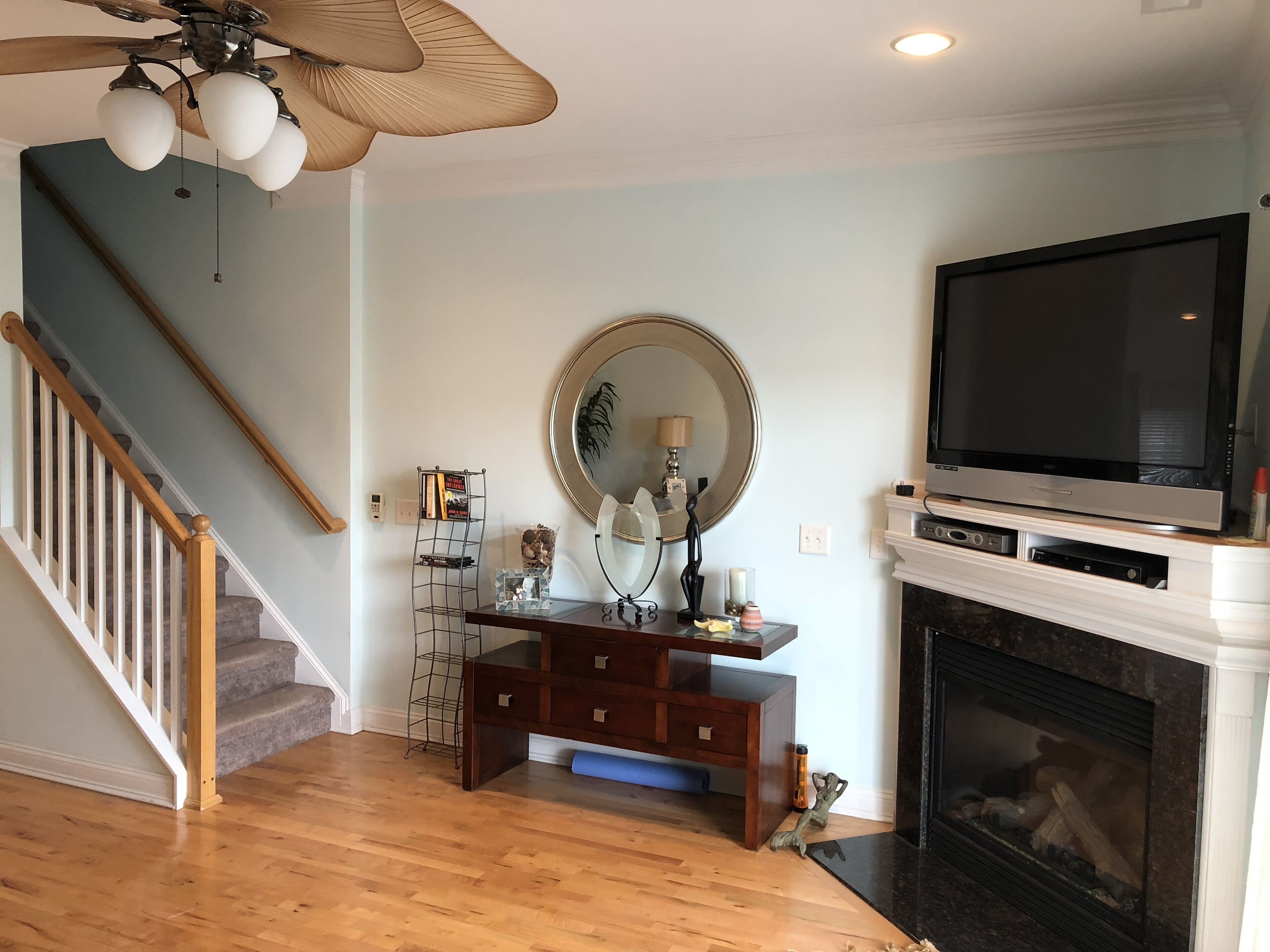 A living room with a wooden staircase, a fireplace, a television, and a ceiling fan.