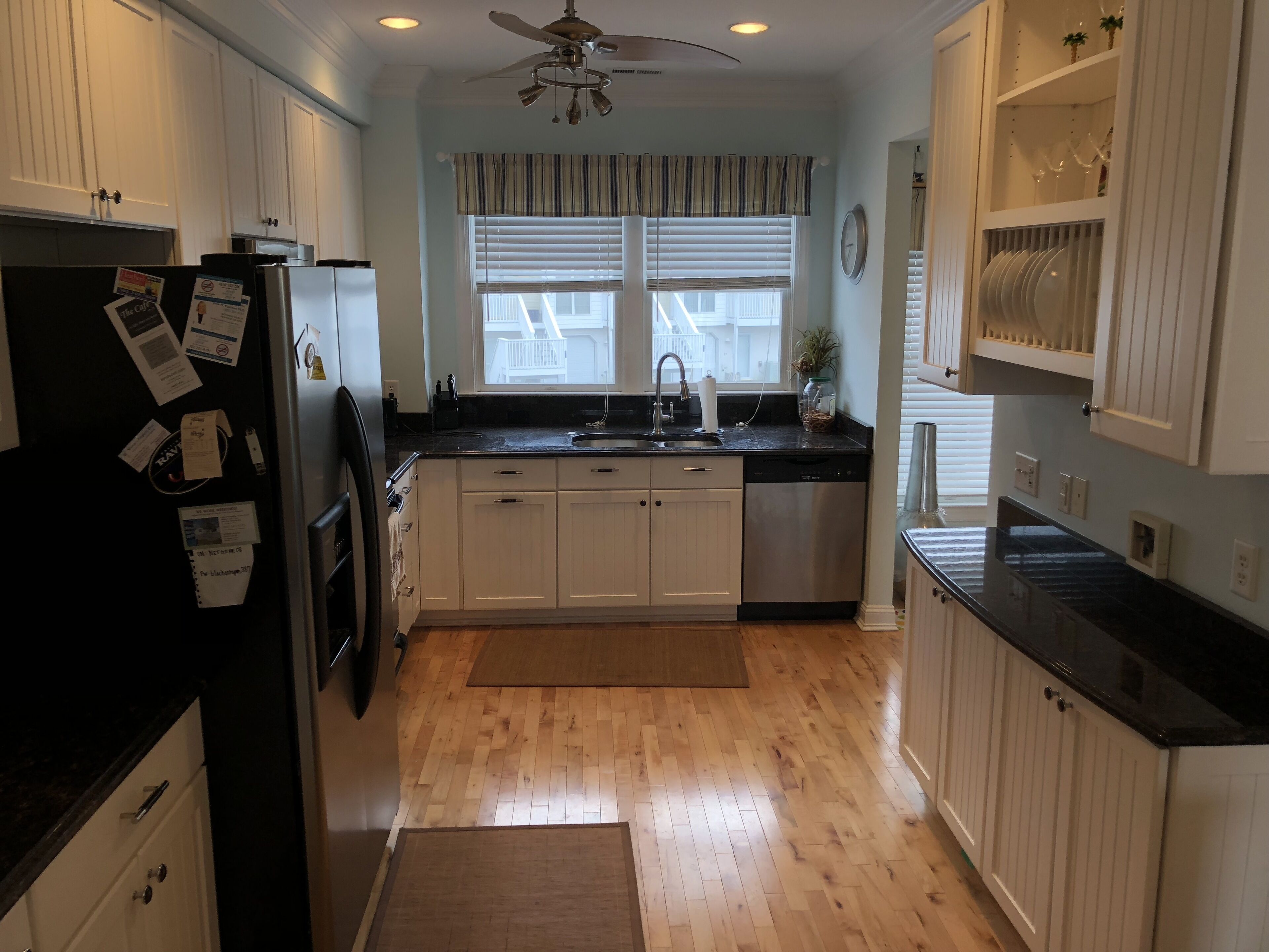 A kitchen with white cabinets, a black countertop, a stainless steel dishwasher, and a ceiling fan.