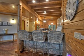 Interior de madera con una zona de bar, sillas de mimbre y un reloj en la pared.