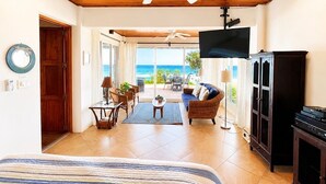 A room with a bed, a ceiling fan, a TV, a wooden cabinet, and a view of the ocean. - Extraordinary Oceanfront Luxury Villa w/Infinity Pool & Full Concierge Service (Playa Negra)