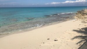 Ein Strand mit klarem türkisblauem Wasser, einem Sandstrand und Felsformationen.