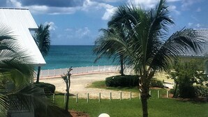 Blick von einem Balkon auf einen Strand mit Palmen und einem weißen Zaun.