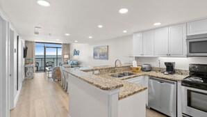 A modern kitchen with granite countertops, stainless steel appliances, and a large island. - Luxurious Oceanfront Condo- Right on the Beach (Windy Hill)