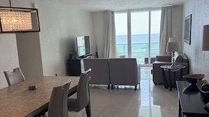 A modern hotel room with a dining area, a sofa, a TV, and a view of the ocean.