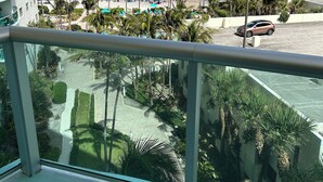 A balcony with a view of a beach, palm trees, and a parking area.