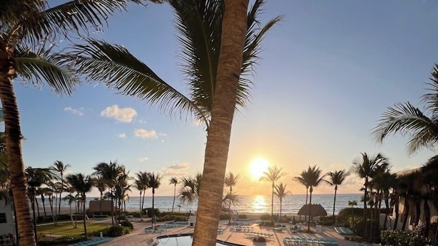 A resort pool area with multiple swimming pools, palm trees, and a sunset view.