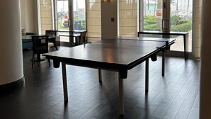 A spacious indoor area with a ping pong table, seating, and large windows.