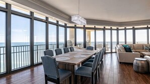 Una habitación amplia con una gran mesa de comedor, varias sillas y vista al mar a través de amplios ventanales.