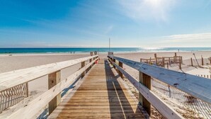Un muelle de madera que lleva a una playa con cielos despejados y aguas tranquilas.