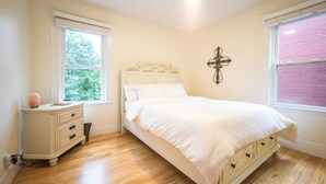 A bedroom with a bed, a nightstand, a dresser, a window, and a wall decoration.