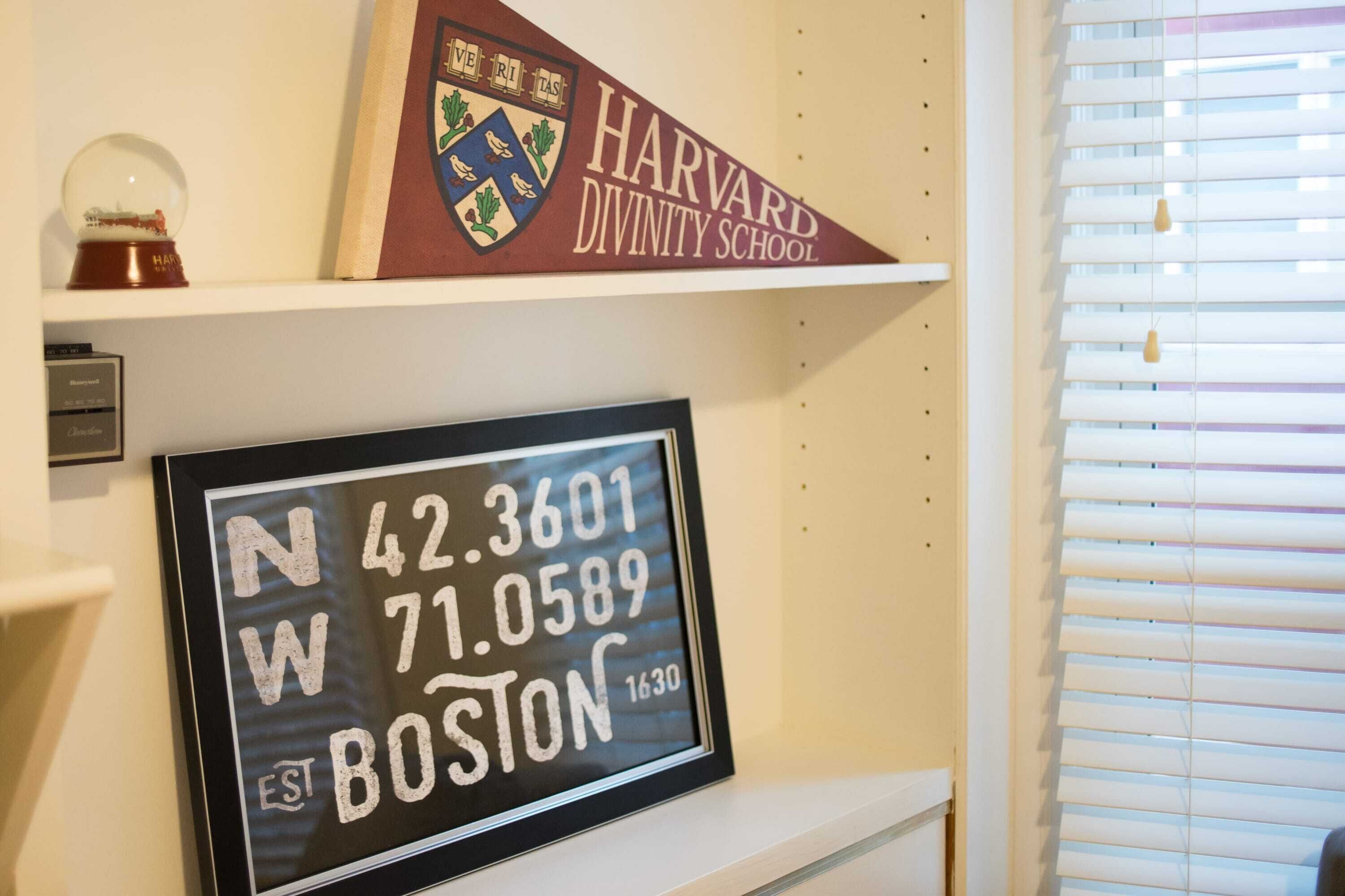 A framed sign with coordinates and the text 'N 42.3601 W 71.0589 EST BOSTON 1630' on a wall.