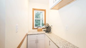 A narrow kitchen with a window, a coffee machine, and a basket on the counter.