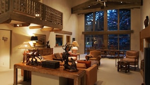 Amplia sala de estar con techo alto, vigas de madera y grandes ventanales que ofrecen vistas al exterior.