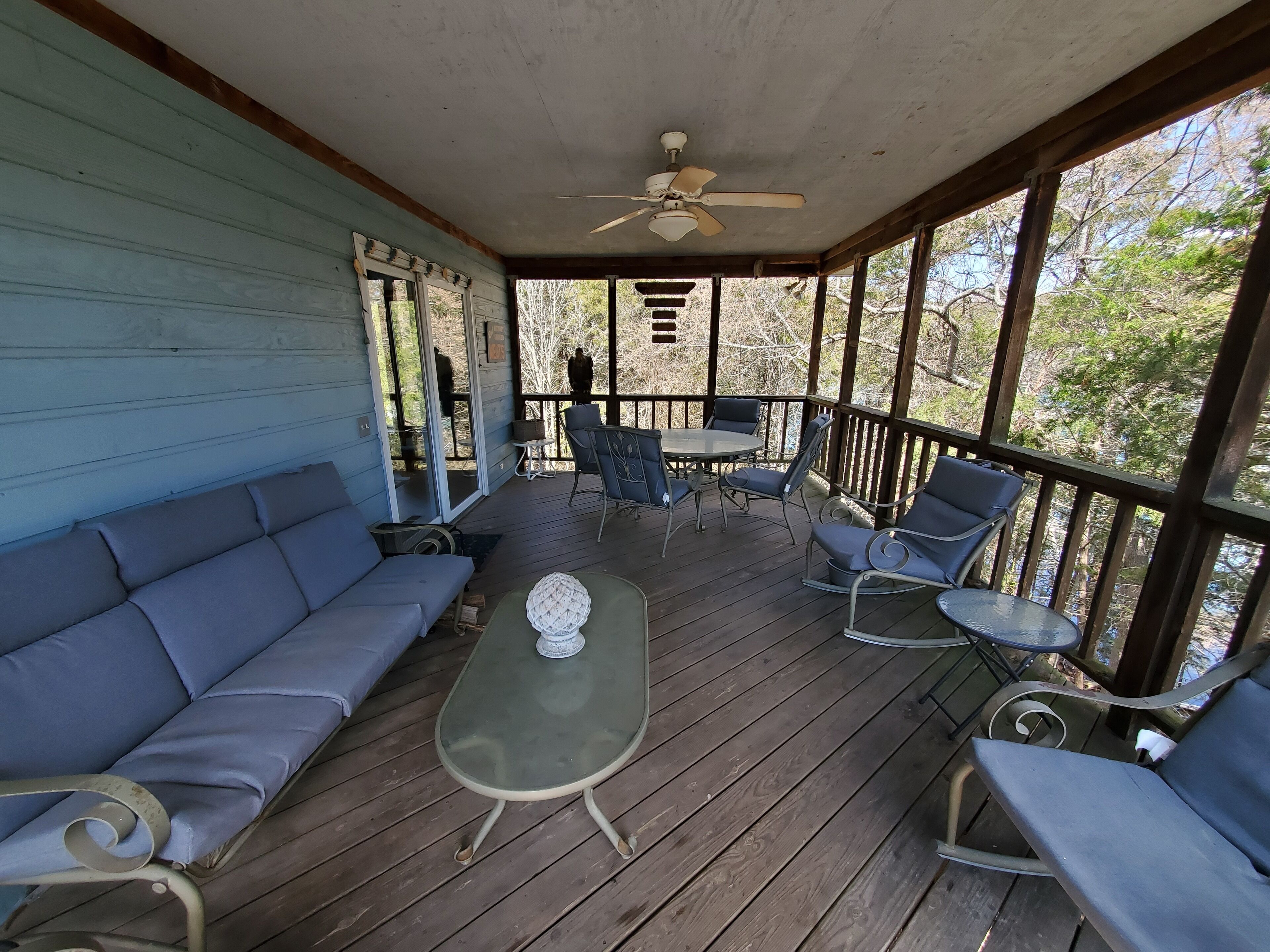 A covered porch with a wooden floor, a ceiling fan, a sofa, a table, and outdoor seating.