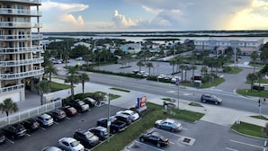 A multi-story hotel with a parking lot, a view of the surrounding area, and a body of water in the background. - Beautiful Florida Condo in Oceanfront Building with River and Ocean Views (Daytona Beach Shores)