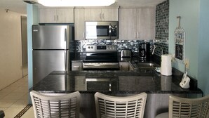 A modern kitchen with stainless steel appliances, a microwave, and a tiled backsplash. - Beautiful Florida Condo in Oceanfront Building with River and Ocean Views (Daytona Beach Shores)