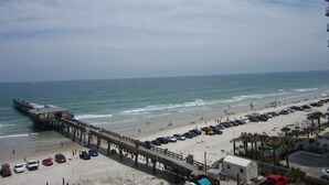 A beach with a pier extending into the ocean, a parking area, and a few buildings. - Beautiful Florida Condo in Oceanfront Building with River and Ocean Views (Daytona Beach Shores)