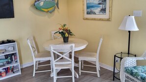 Un comedor con una mesa redonda y cuatro sillas, una estantería, una decoración de pez, un cuadro enmarcado y una lámpara.