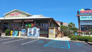 Un edificio frente a la playa con letreros que dicen 'WAVES' y 'WAVES BEACH SUPPLIES & GROCERIES'.