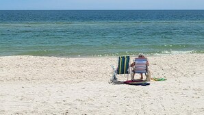 Una playa con cielo despejado, mar tranquilo y una persona en silla de ruedas cerca de una silla de playa.
