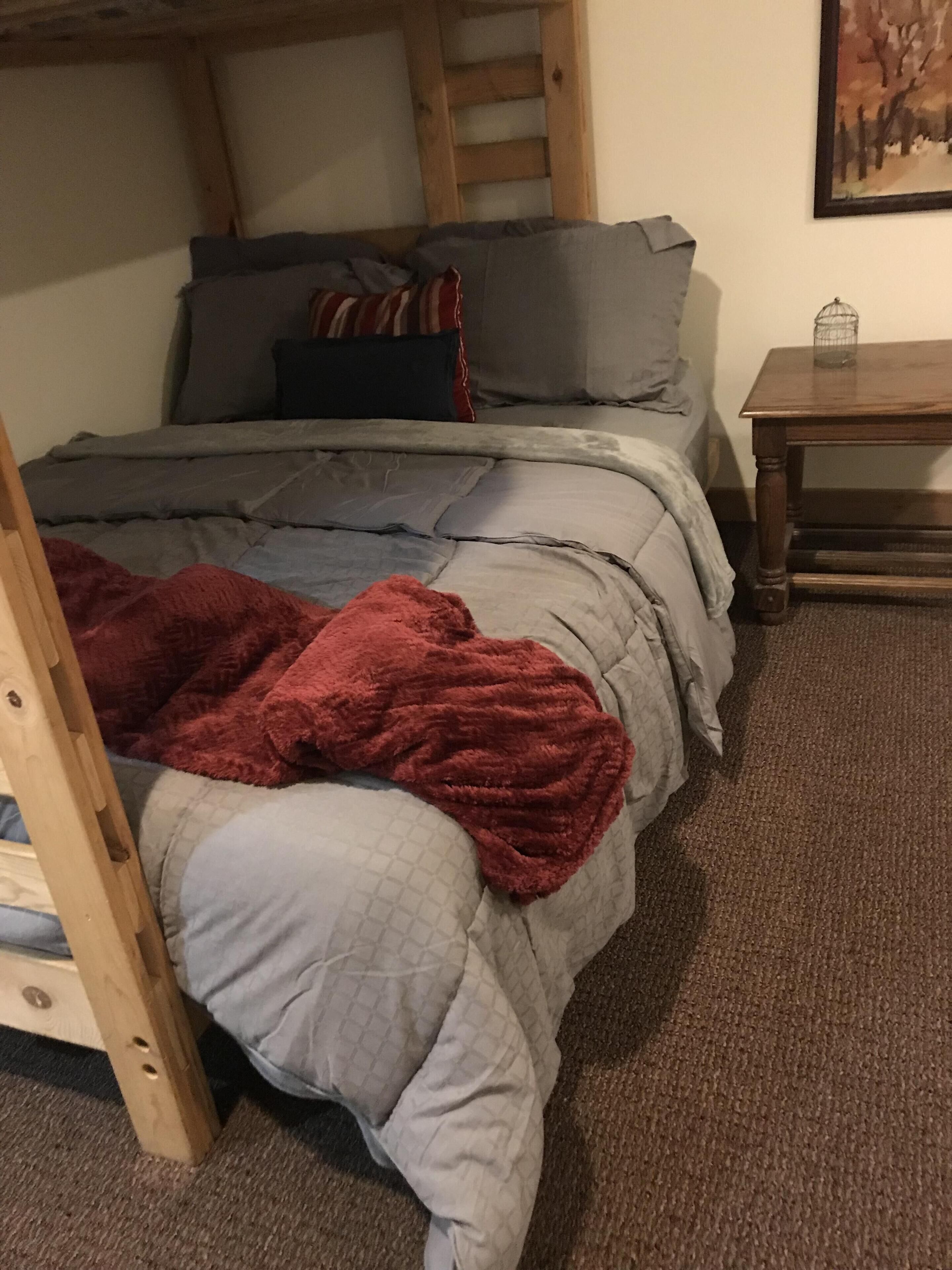 A bunk bed with a red blanket, grey bedding, and a wooden ladder.