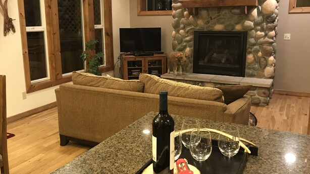 Een woonkamer met een stenen openhaard, een televisie en een eetgedeelte met een granieten aanrecht en wijnglazen.