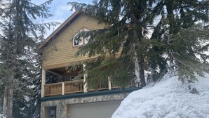 Een huis met twee verdiepingen en een balkon, omringd door sneeuw en bomen.