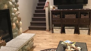 Een woonkamer met een stenen openhaard, een televisie, een trap en een salontafel met decoratieve objecten.