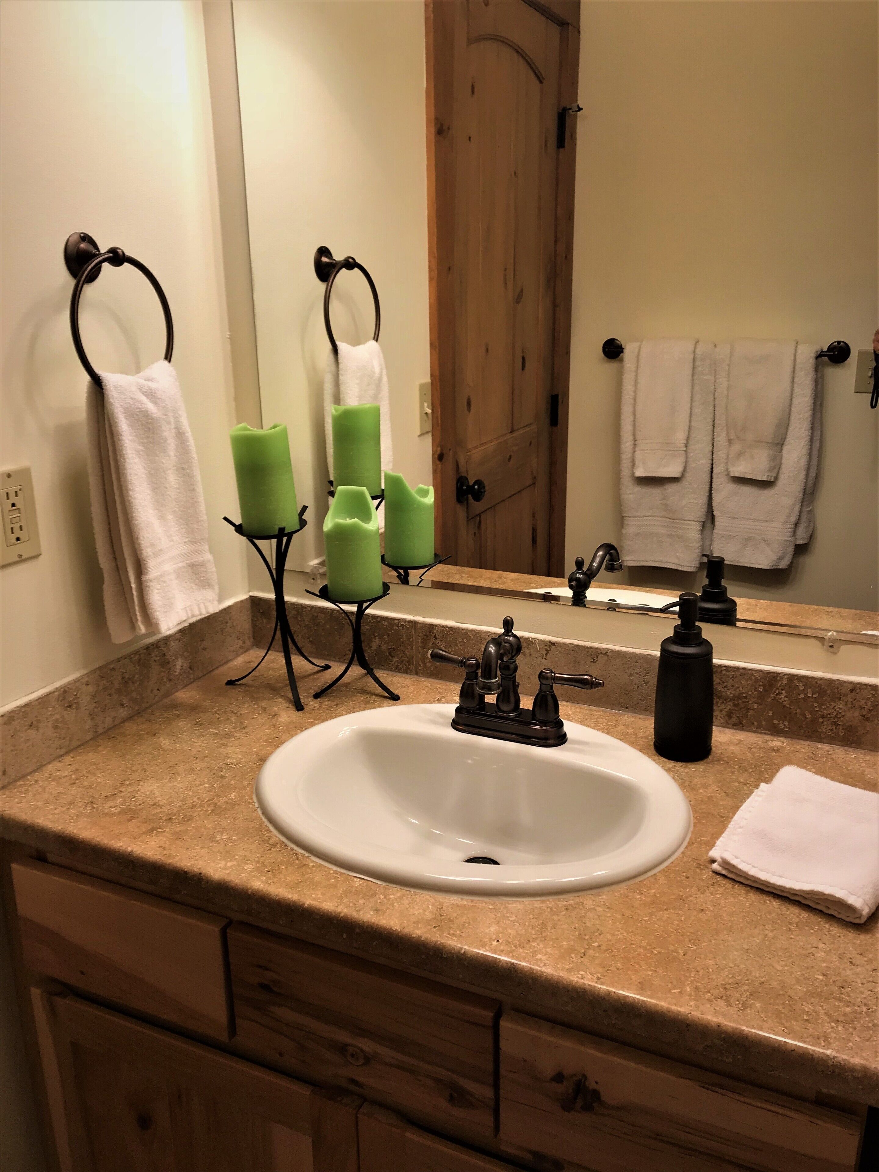 A bathroom with a white sink, a mirror, a wooden door, and a towel rack with white towels.