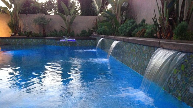 A swimming pool with a waterfall feature, surrounded by tropical plants and a tiled wall. - VACATION HOME HAVE POOL & SPA / NEAR TO BEACHES-DISNEYLAND. (Huntington Beach)