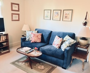 A living room with a blue sofa, a coffee table, a lamp, and framed pictures on the wall.