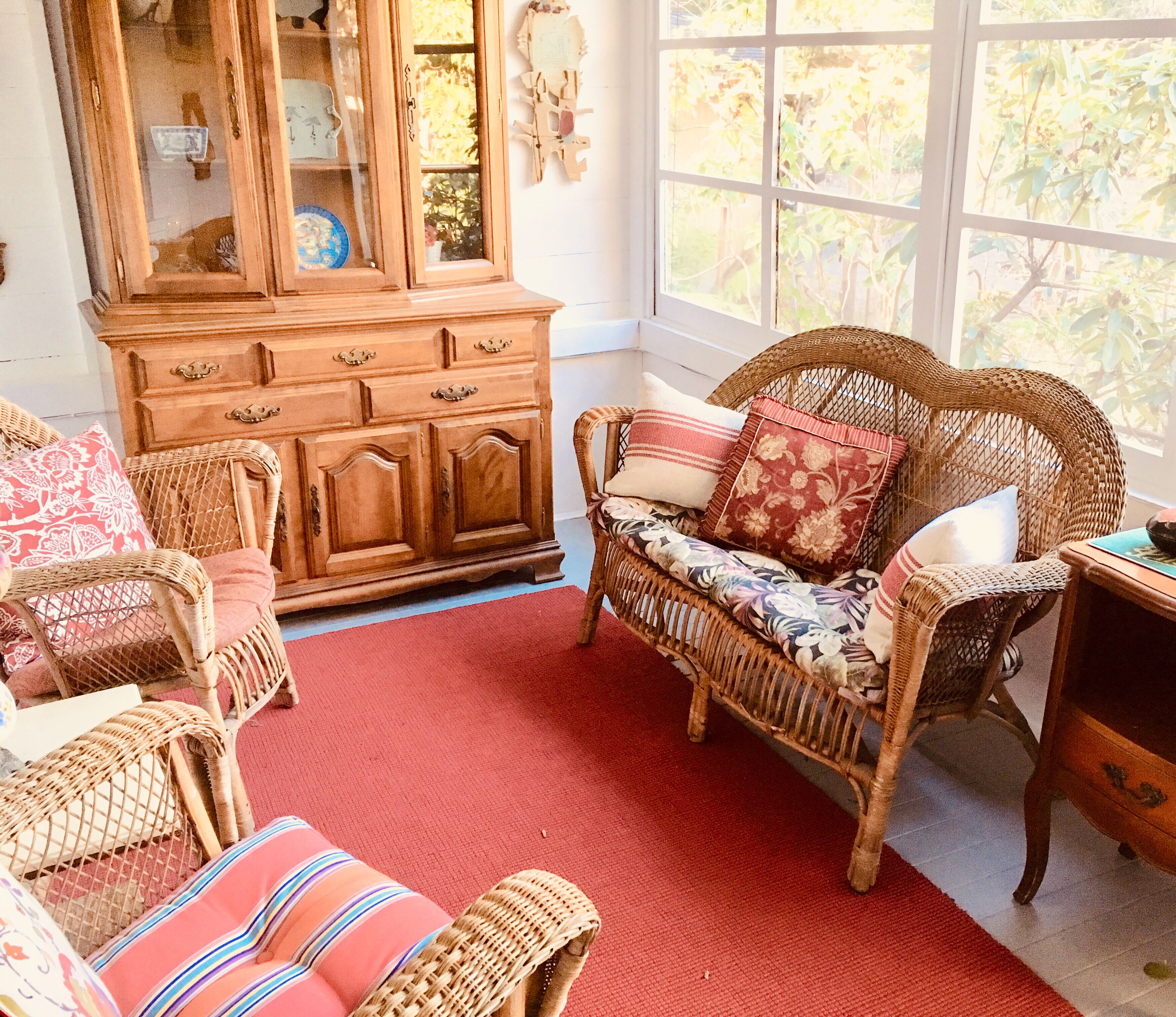 A room with wicker furniture, a red carpet, and a large window with a view of greenery.
