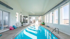 En indendørs swimmingpool med klart, blåt vand, omgivet af hvide vægge og store vinduer.