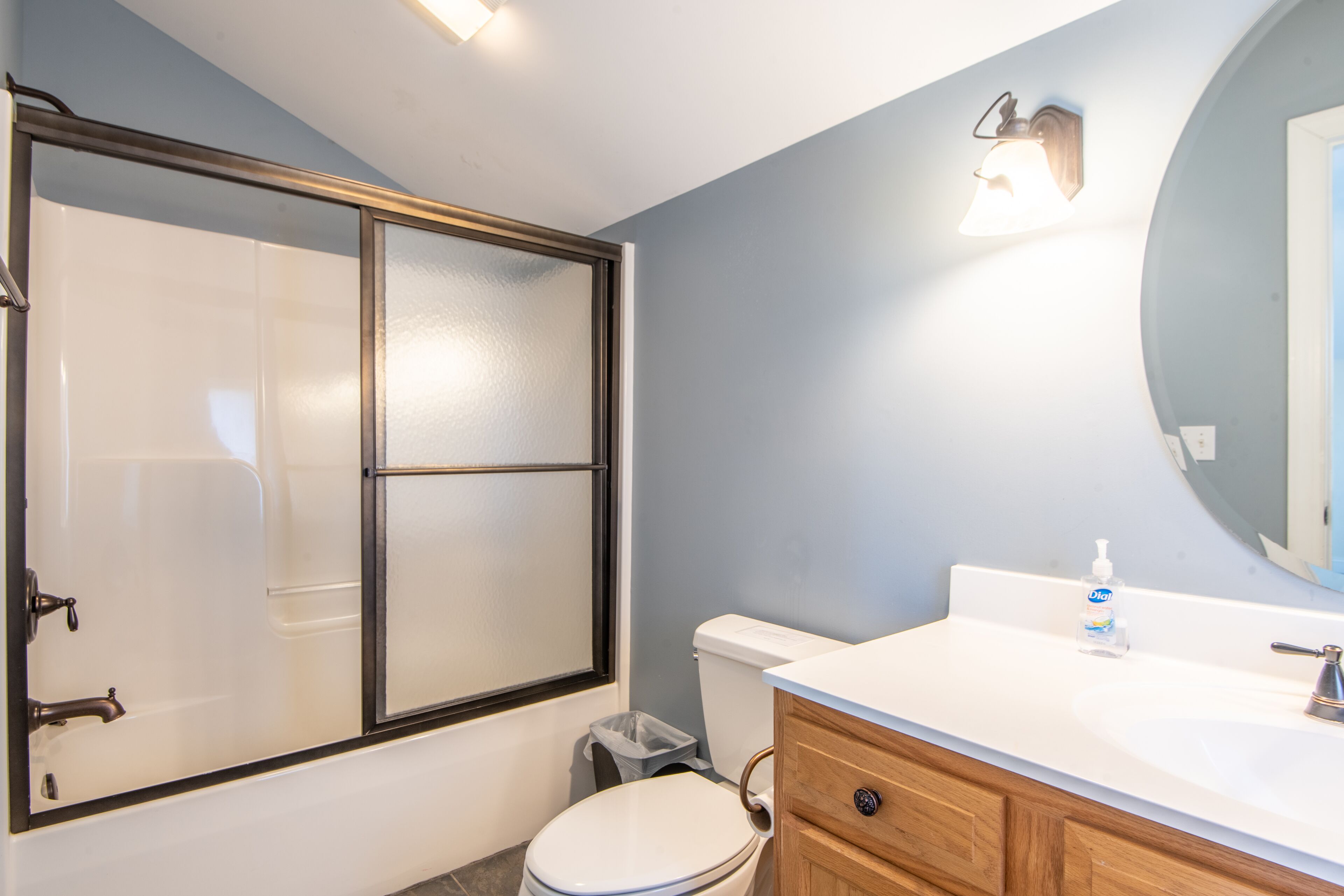 Une salle de bain dotée d’une douche à parois de verre, de toilettes blanches, d’un meuble-lavabo en bois avec un évier et d’un miroir au-dessus du meuble-lavabo.
