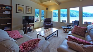 A spacious living room with a large TV, comfortable seating, and a view of a lake.