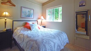 A bedroom with a bed, two bedside lamps, a window, a painting, and a mirror.