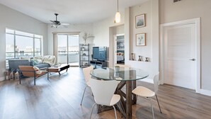 Amplia sala de estar con mesa de comedor de vidrio, muebles modernos y grandes ventanales con vistas a la ciudad.