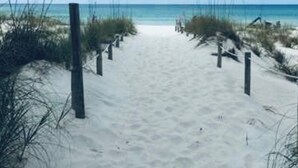 Un sentier de sable qui longe la plage et mène à l’océan, avec des poteaux en bois de chaque côté.