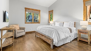 Ein Schlafzimmer mit einem großen Bett, Holzboden und einem Fenster mit Blick auf ein Haus und Bäume.