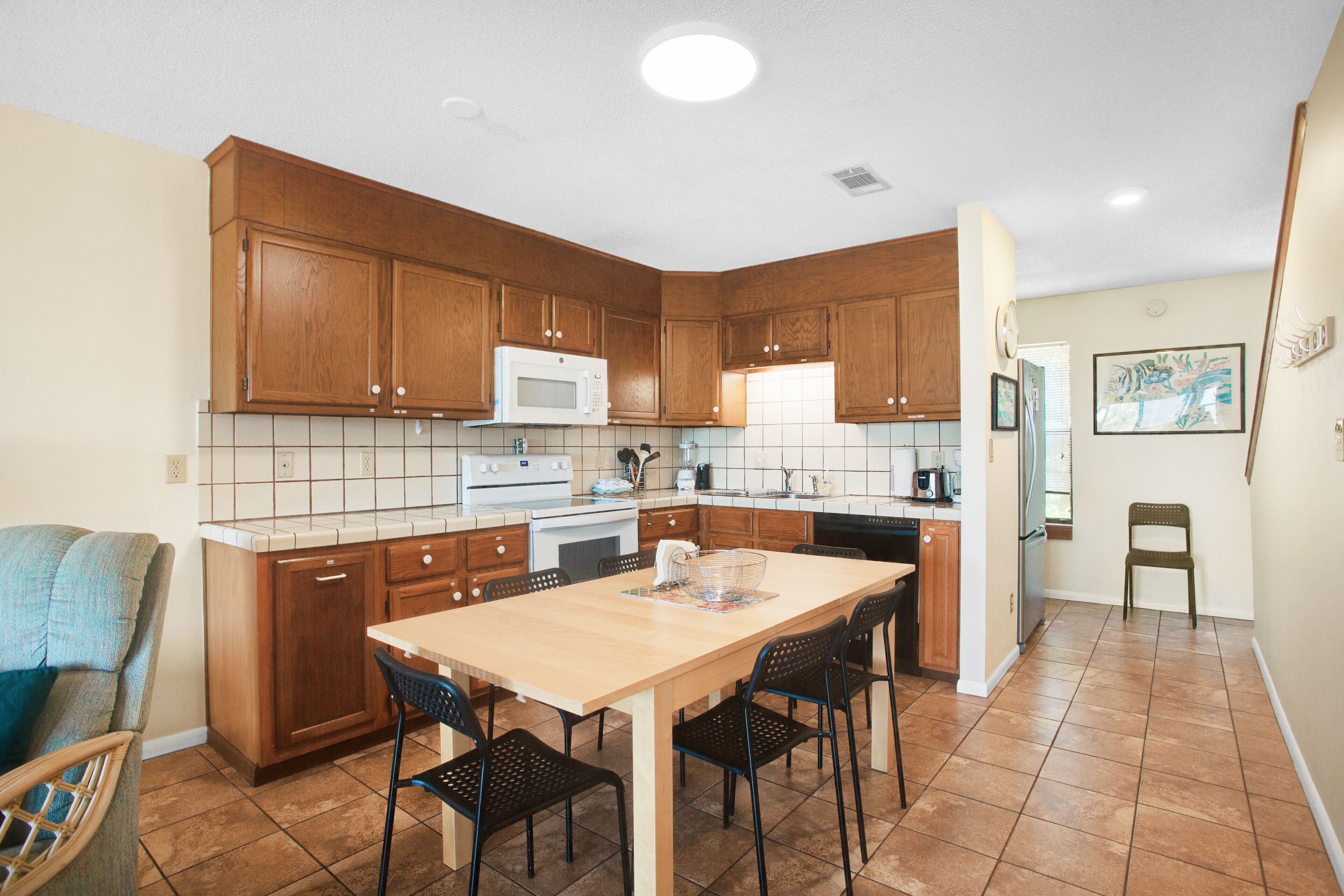 Une cuisine avec des meubles de rangement en bois, un four à micro-ondes blanc, une cuisinière et une table à manger avec des chaises.