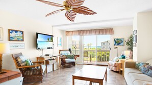 A spacious living room with a large wooden table, wicker chairs, a sofa, and a ceiling fan.