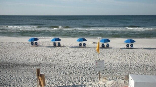 A beach with four blue umbrellas and lounge chairs, a sandy shore, and the ocean in the background.